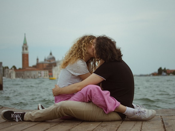 A man and a woman sitting on a pier kissing