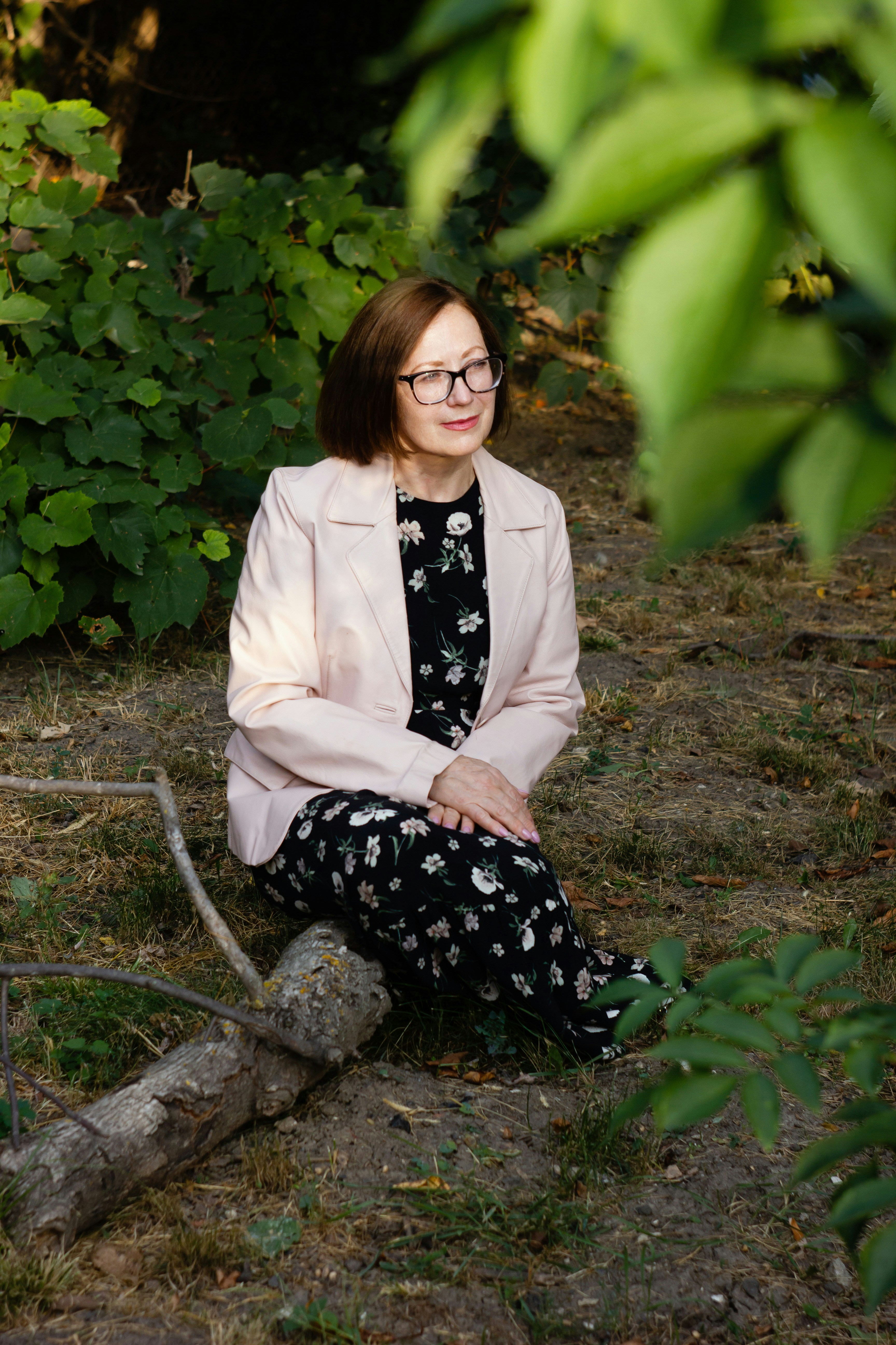 A woman sitting on the ground in front of a bush