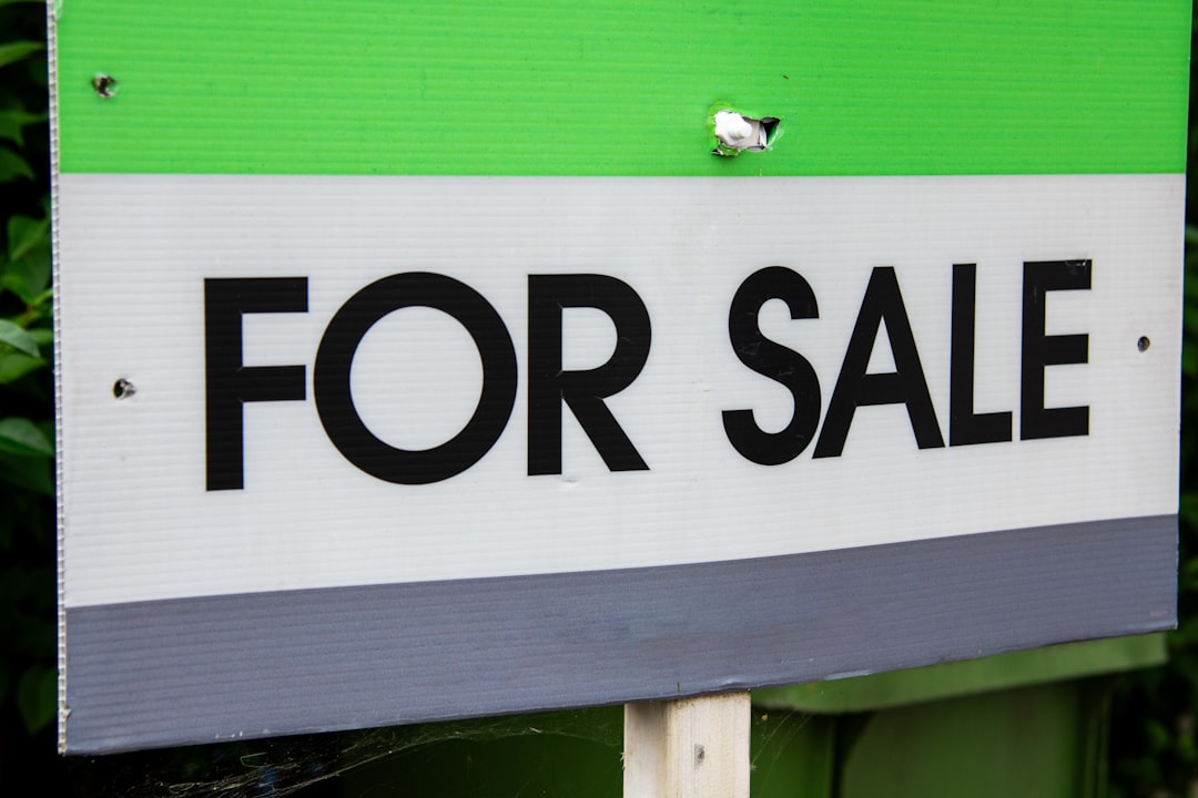 A green and white for sale sign with a bird perched on it,