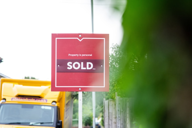 A red sold sign at the edge of a residential road, marking a completed home sale