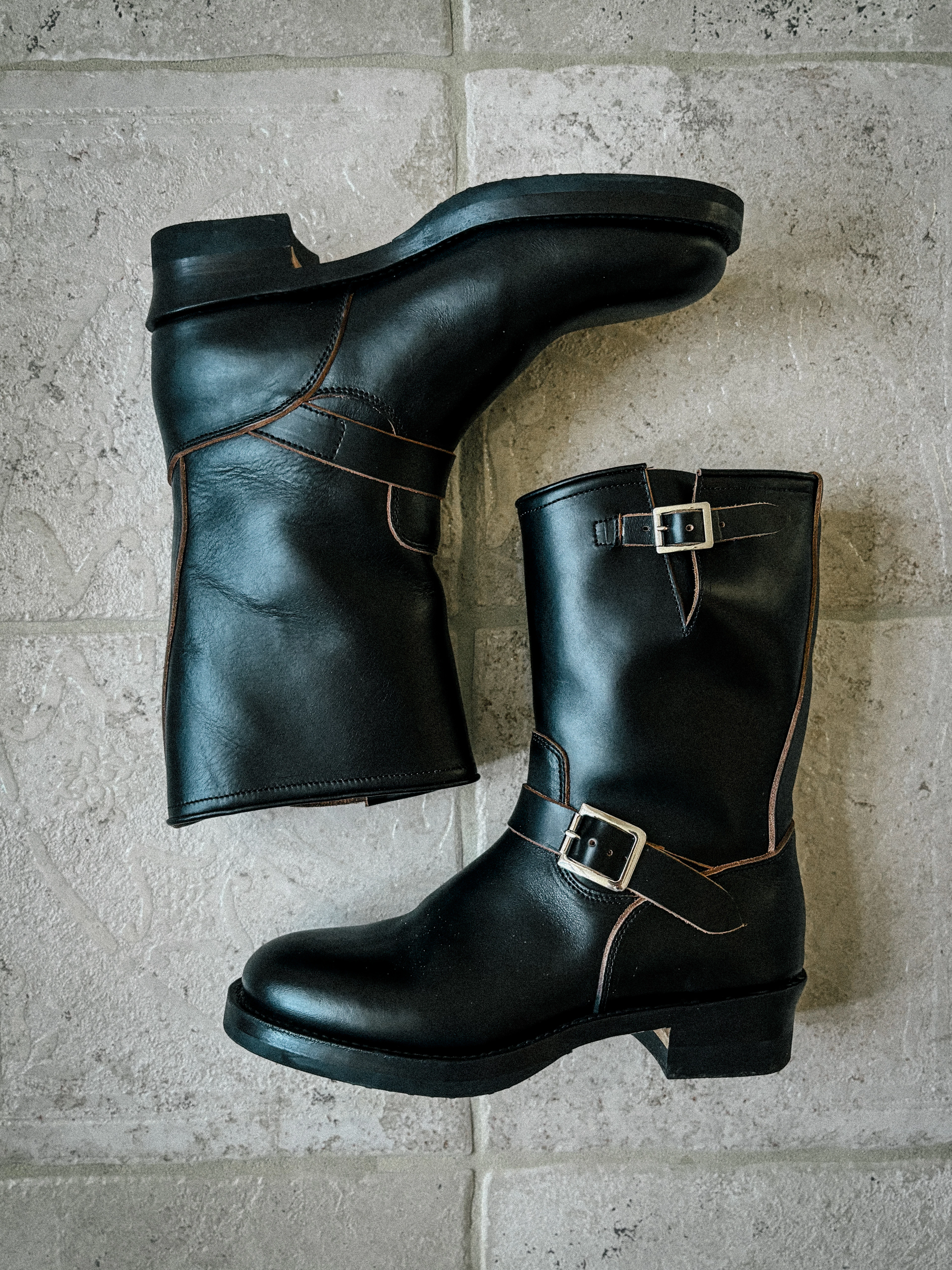 A pair of black leather engineer boots with buckled straps, laid on a stone floor