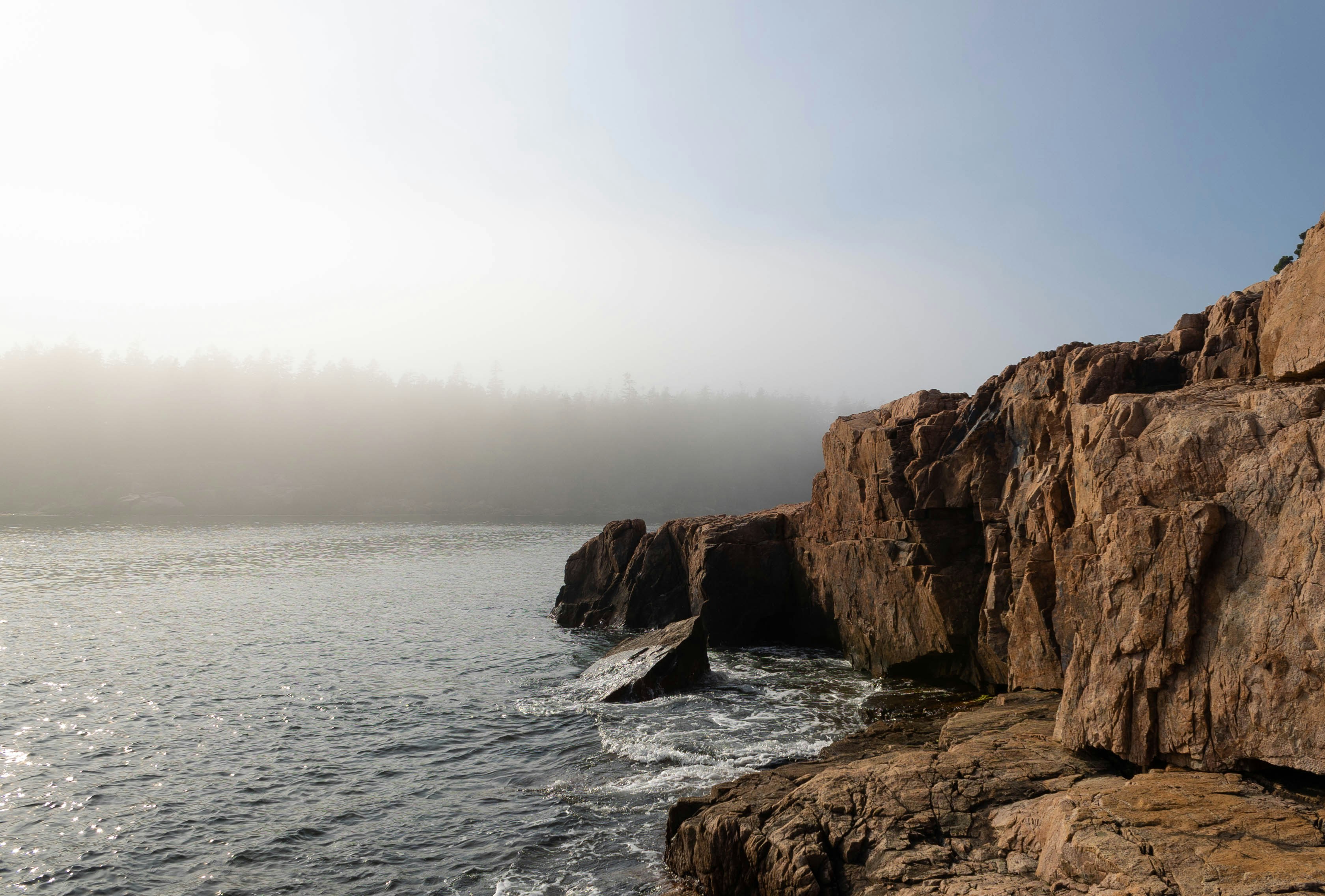 Person standing on a rocky coastal cliff overlooking the Atlantic Ocean in Acadia National Park.
