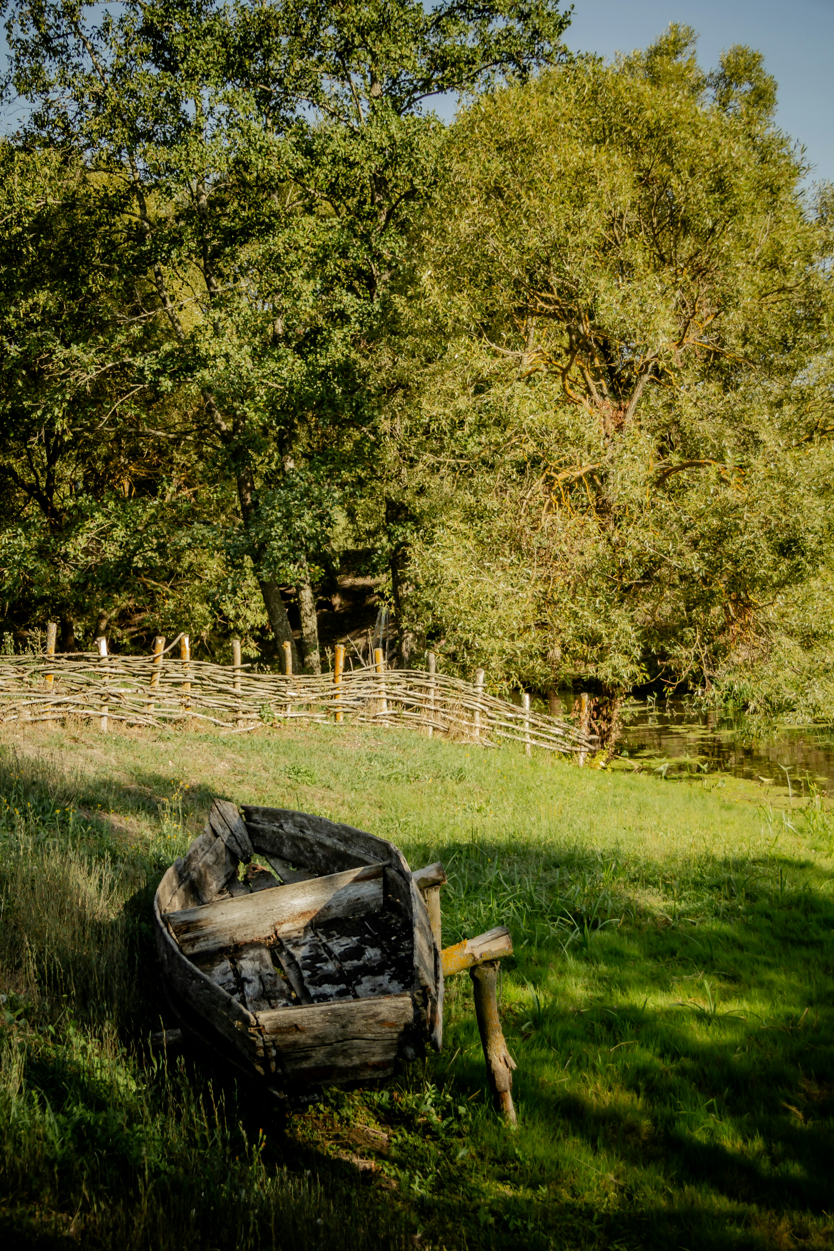 An old boat sitting in the grass near a fence