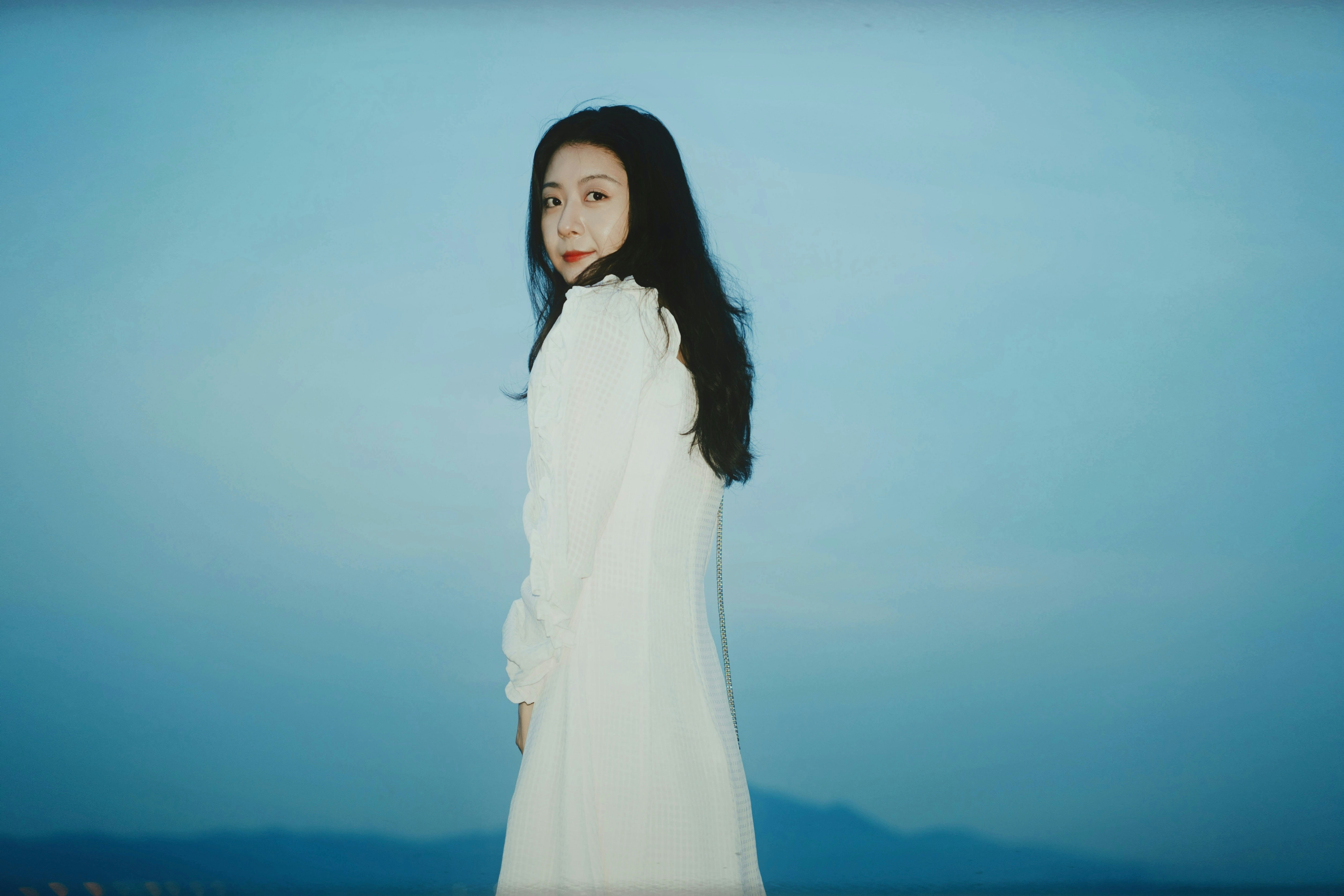 A woman in a white dress standing in front of a blue sky