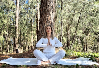 A woman sitting in the middle of a forest doing yoga