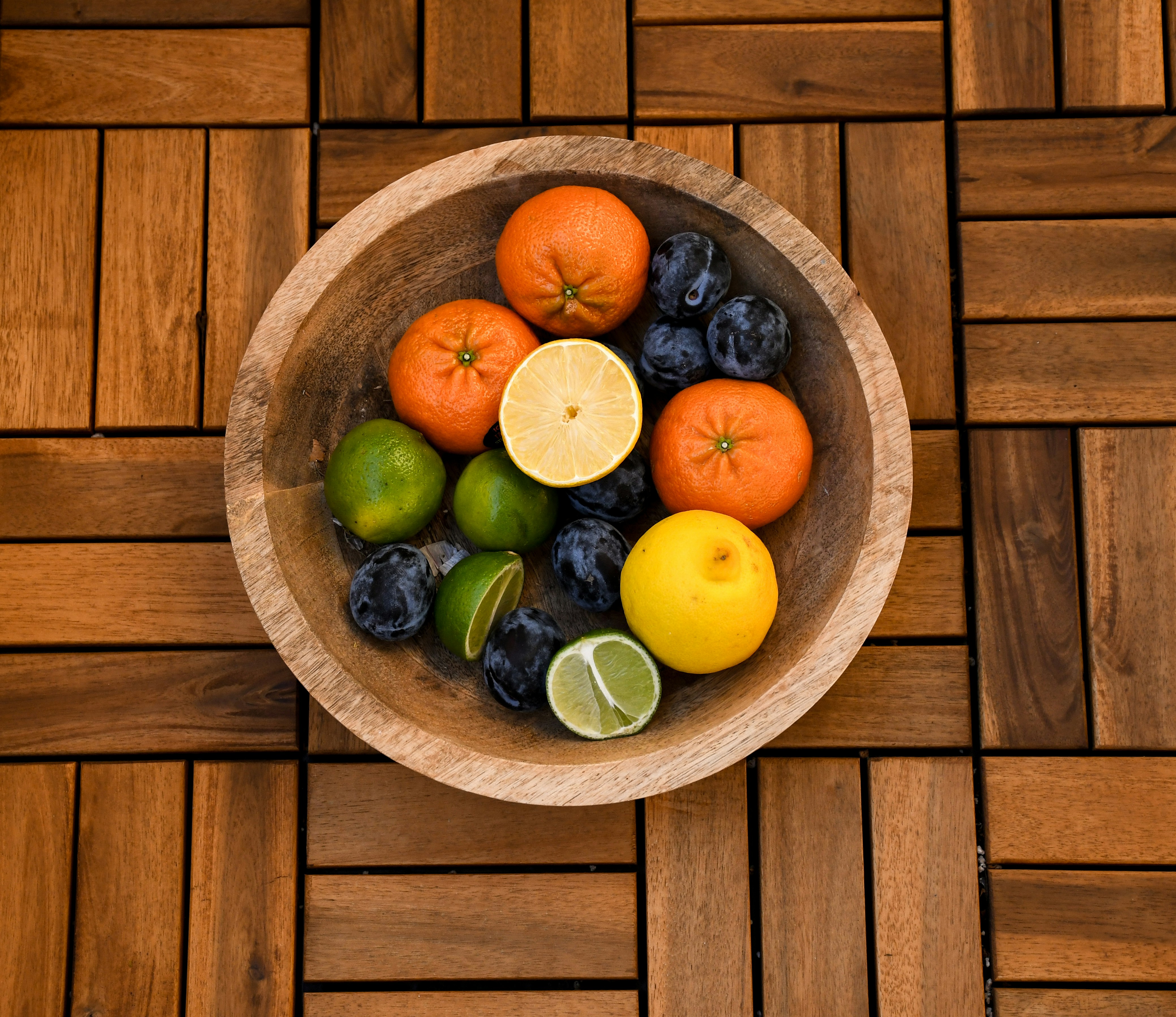A wooden bowl filled with fruit on top of a wooden floor