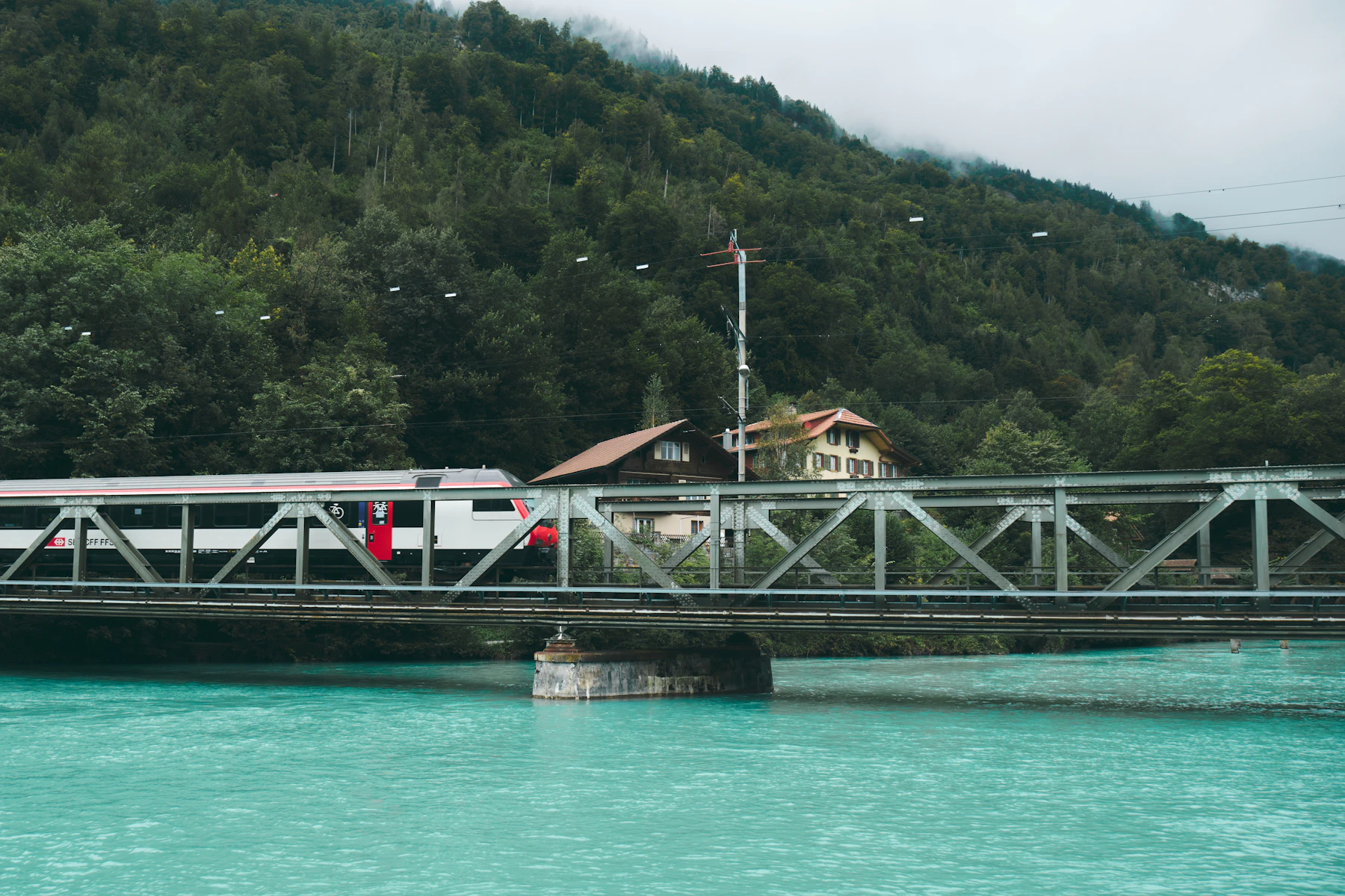 A Swiss passenger train crossing a bridge above turquoise water in Interlaken