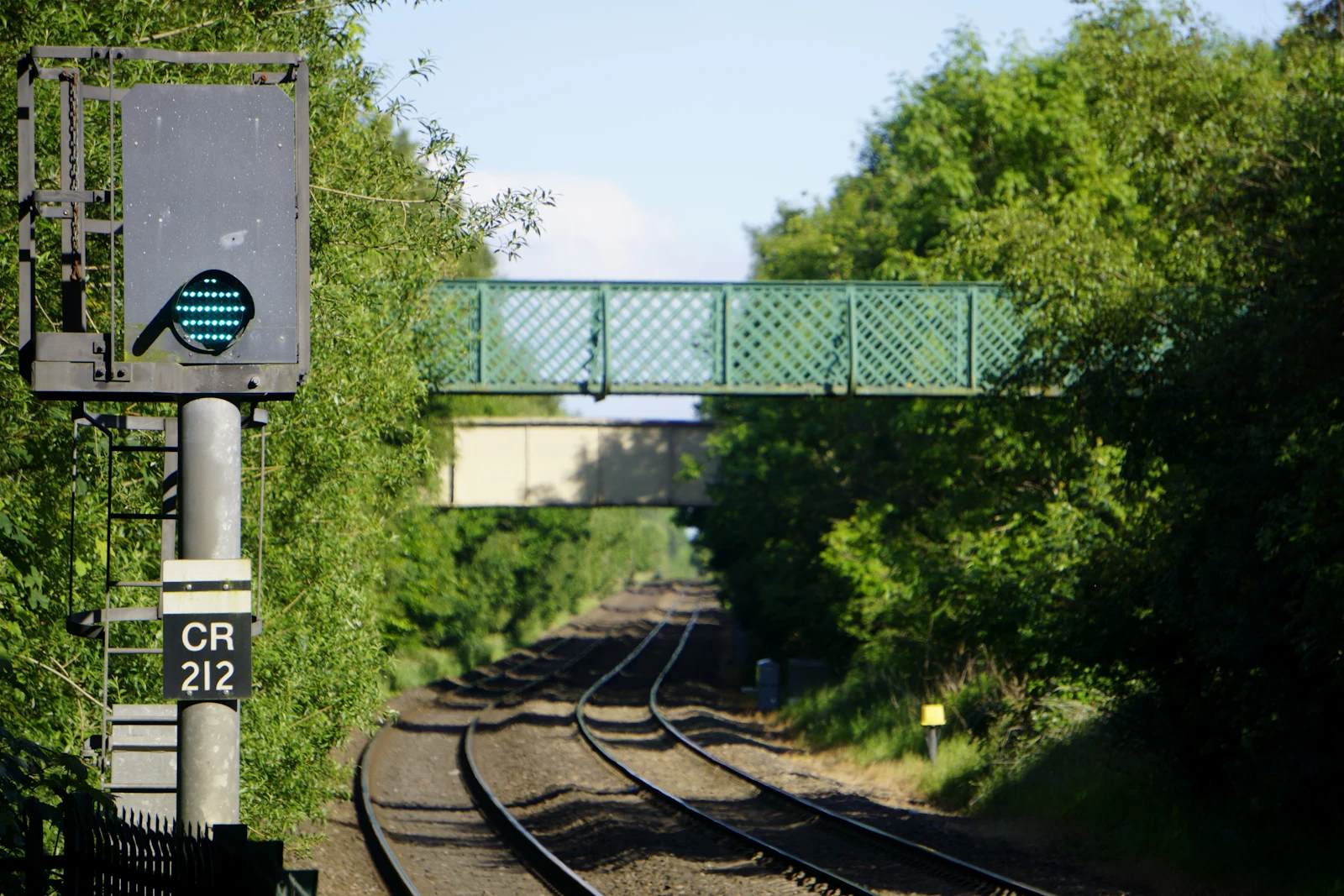 A green railway signal bridge spanning train tracks, showing a proceed aspect on the North Wales Coast line