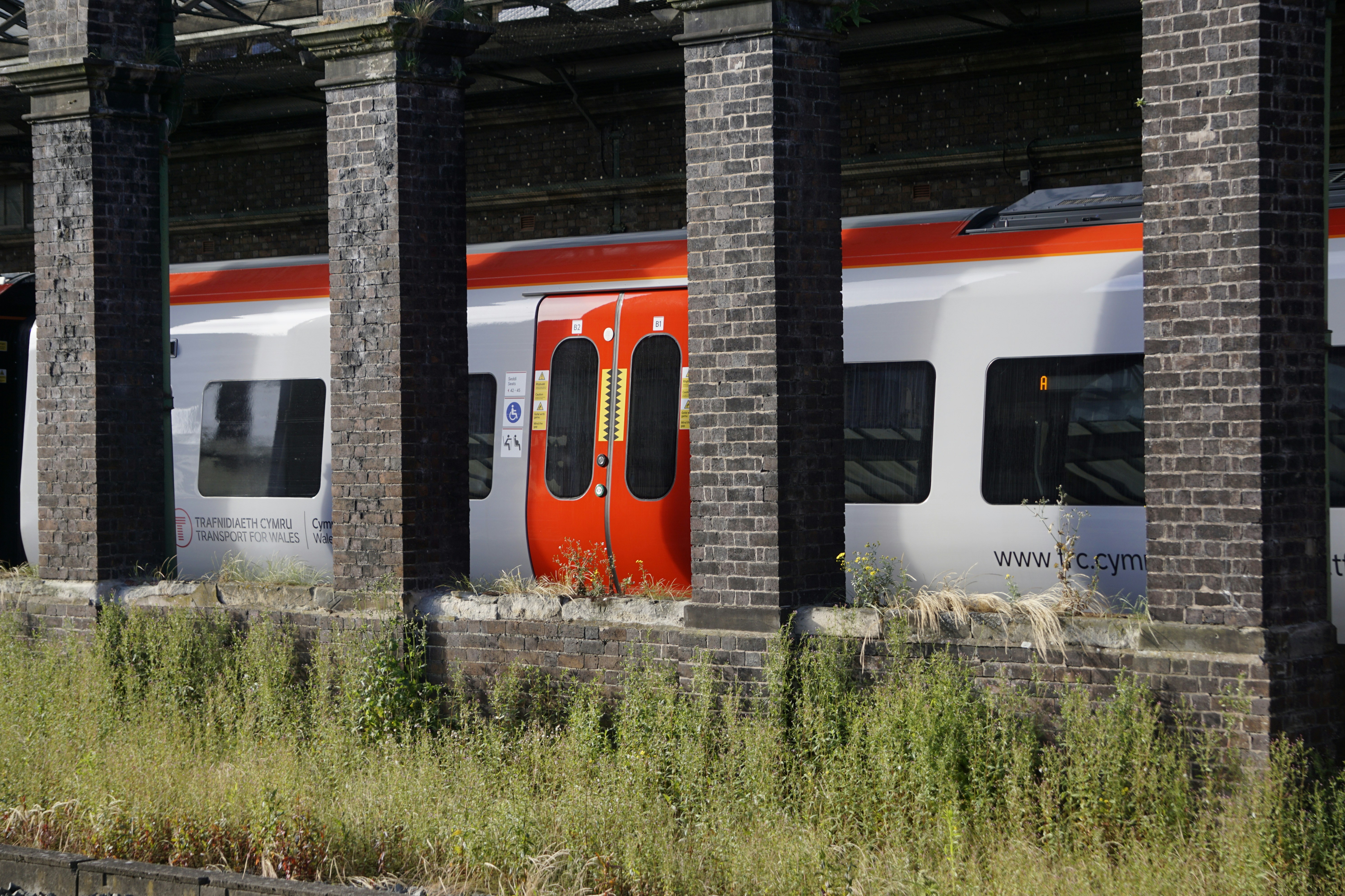 A red and white train traveling past a tall brick building