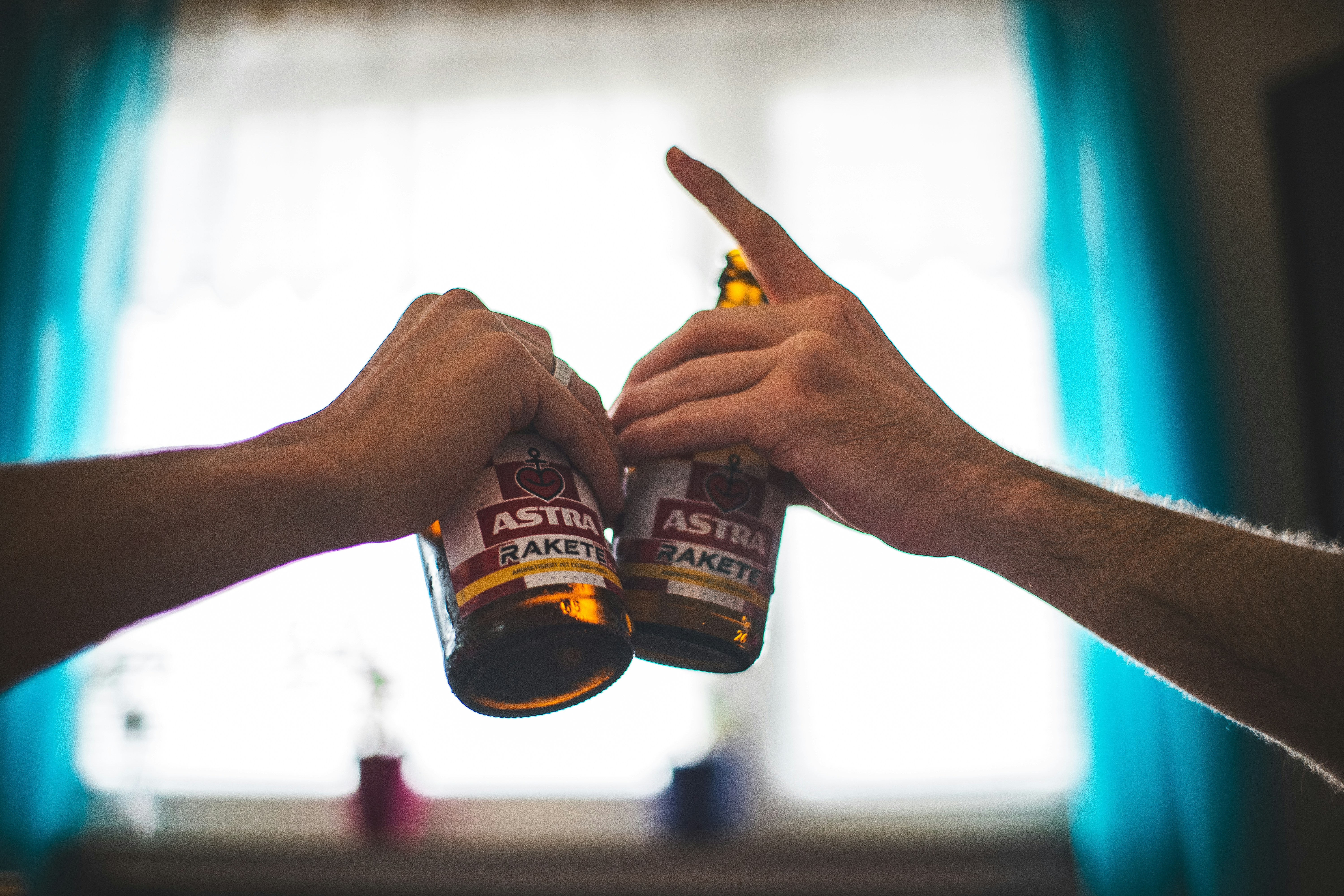 Two people holding beer bottles in front of a window