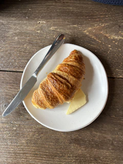 A croissant on a plate with butter and a knife