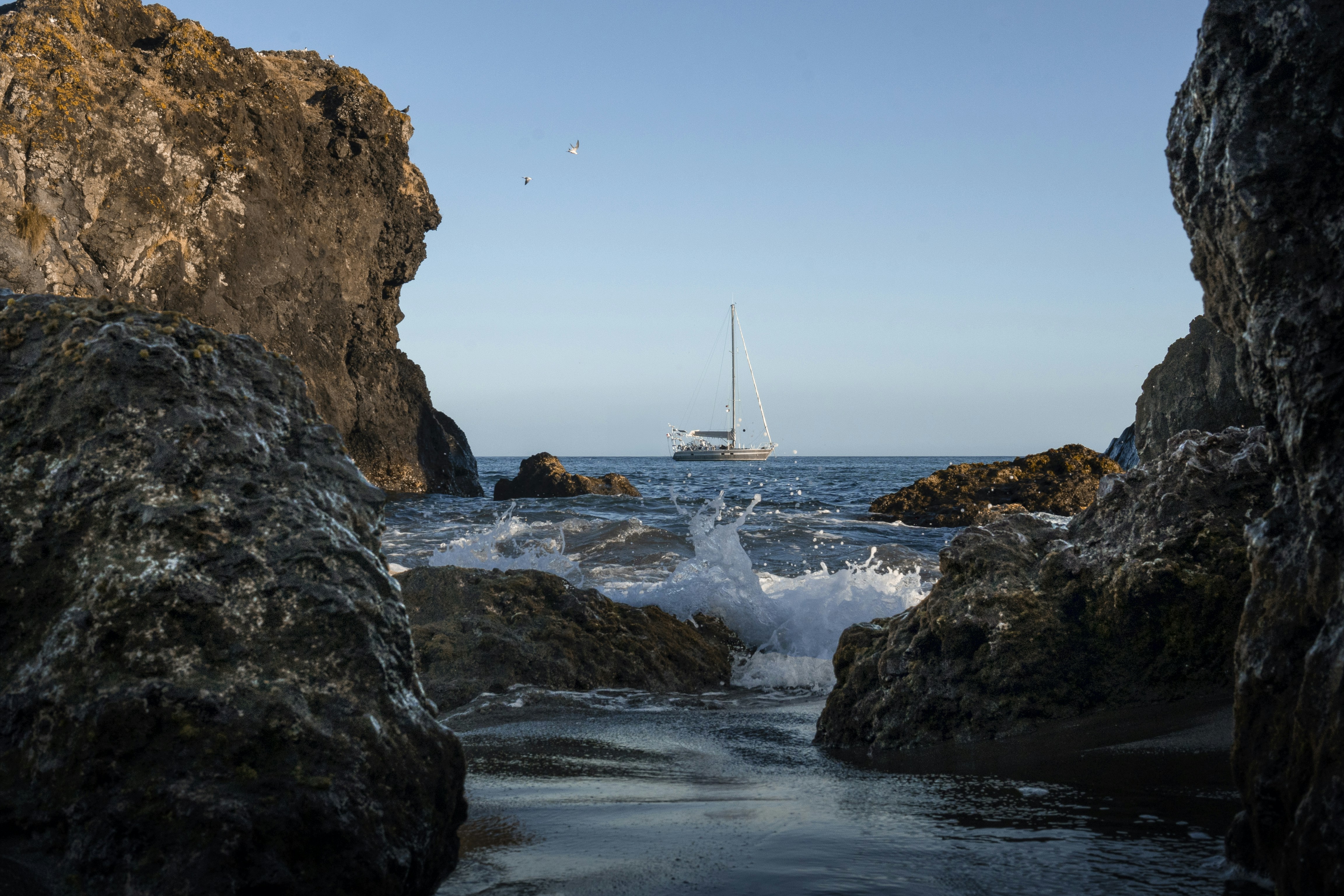 A sailboat is sailing in the ocean through some rocks