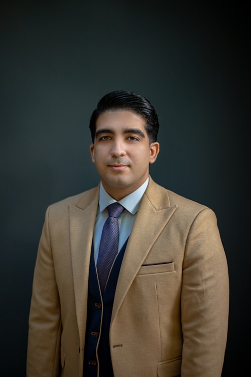 A man in a tan suit posing against a dark background
