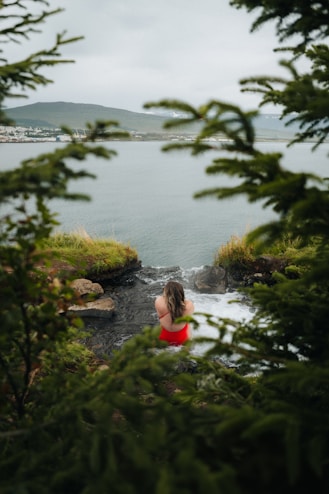 A woman in a red bathing suit sitting on a cliff overlooking a body of water