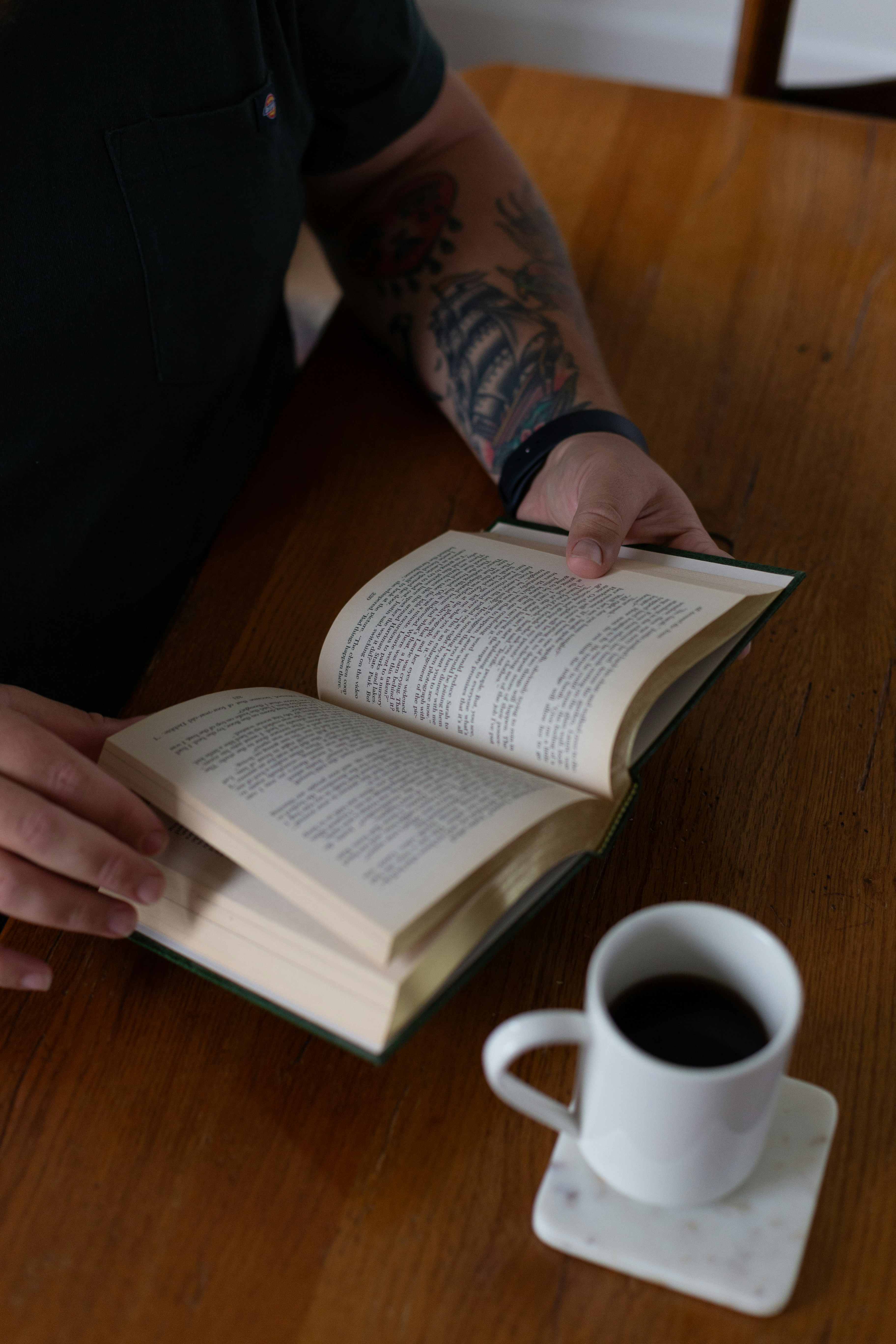 A person sitting at a table with a book and a cup of coffee