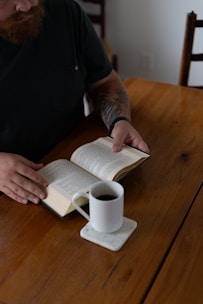 A man sitting at a table with a book and a cup of coffee