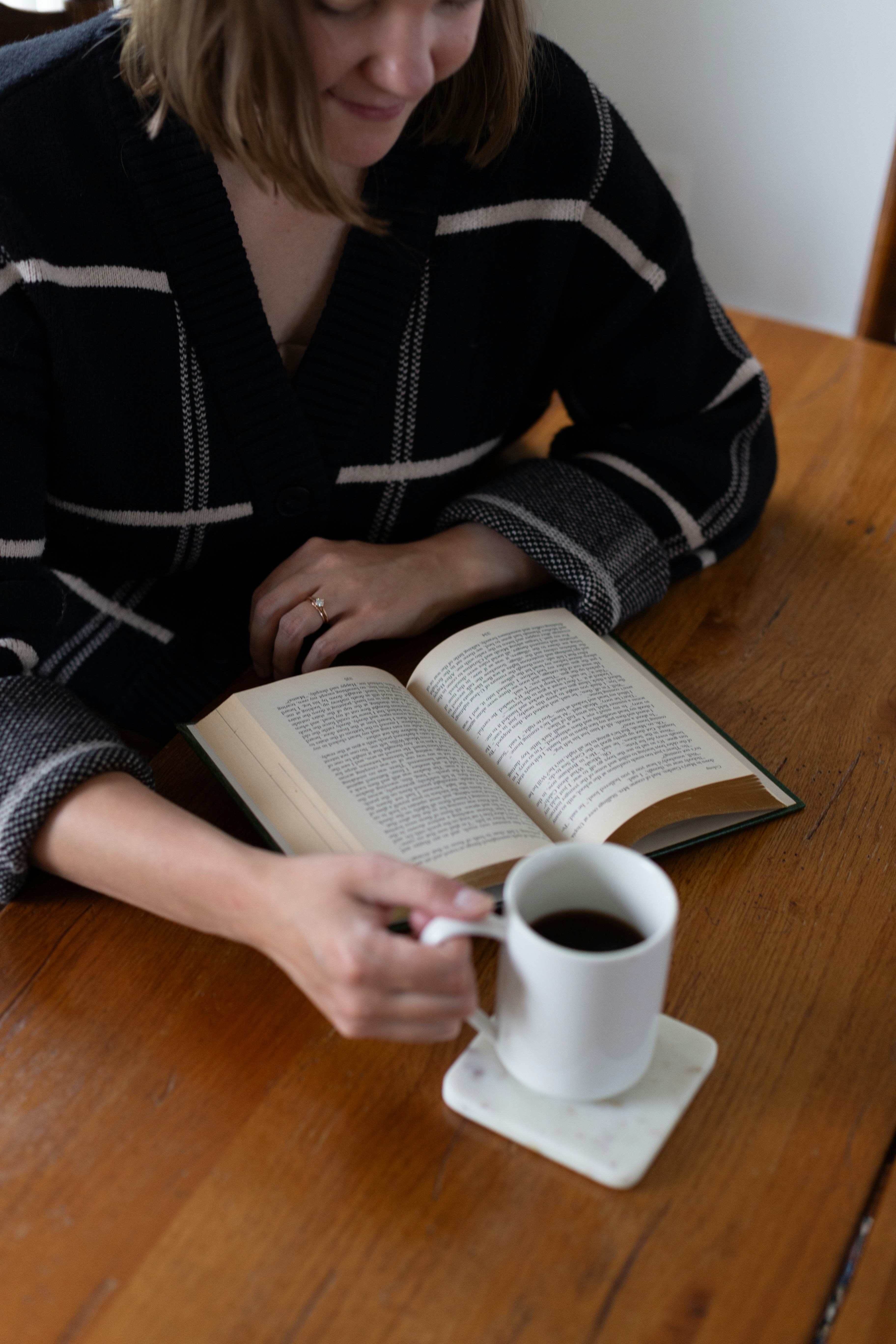 A woman sitting at a table with a book and a cup of coffee