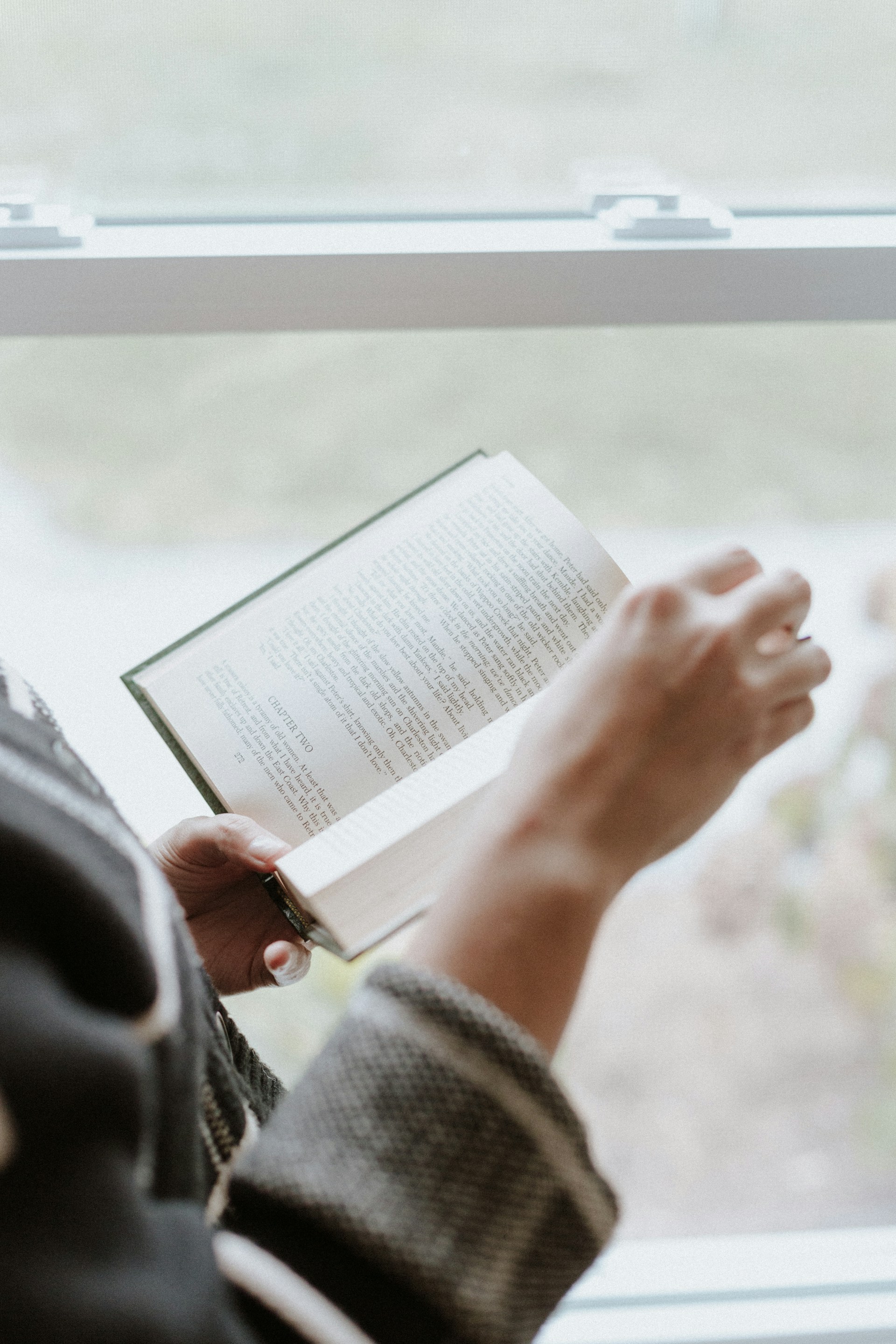 A person reading a book in front of a window