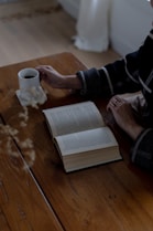 A person sitting at a table with a book and a cup of coffee