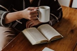 A person sitting at a table with a book and a cup of coffee