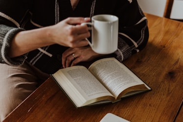 A person sitting at a table with a book and a cup of coffee