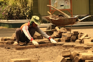 A man laying bricks on the ground in front of a wheelbarrow