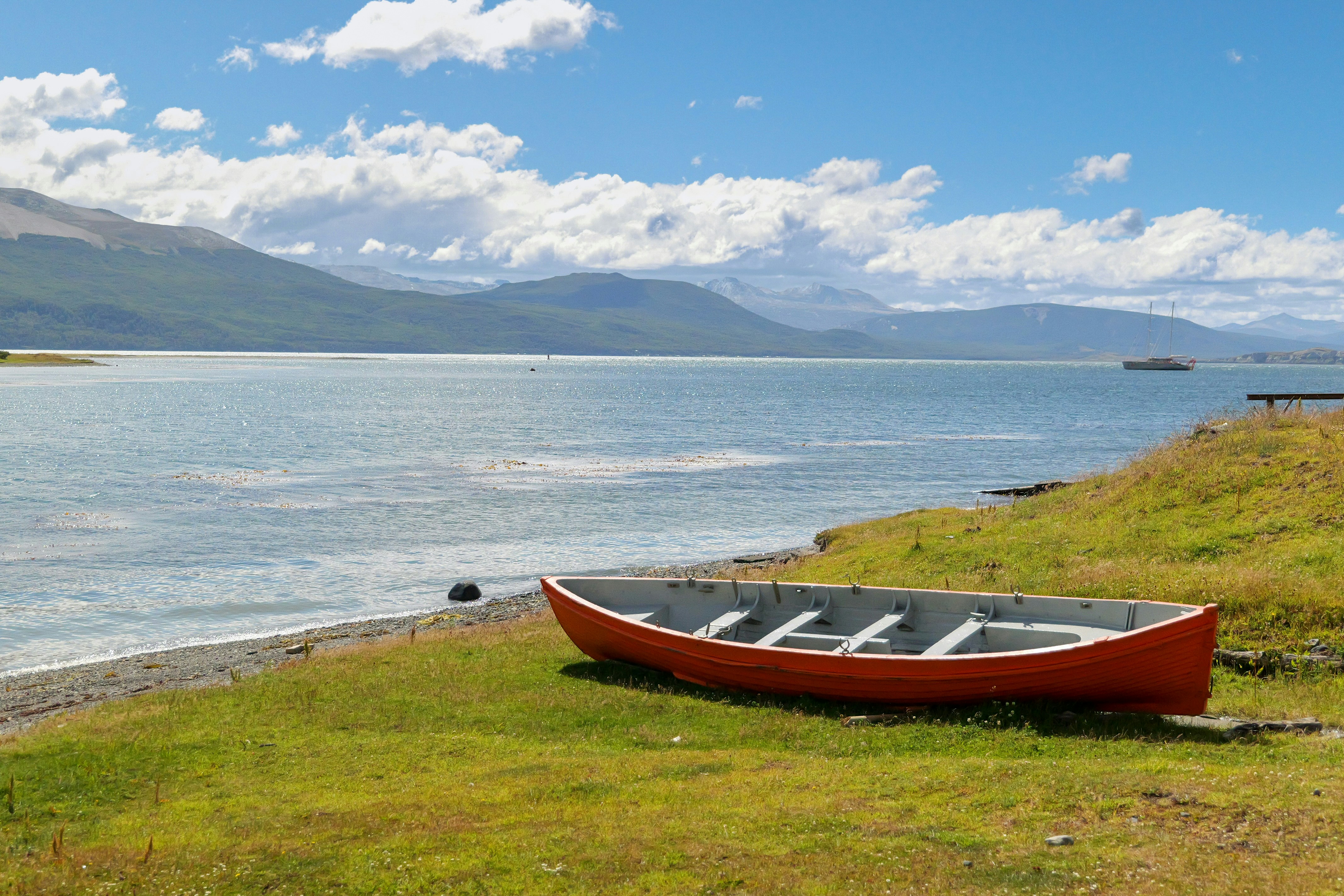 A red boat sitting on top of a lush green field, Red canoe on along Beagle Channel shore in Patagonia