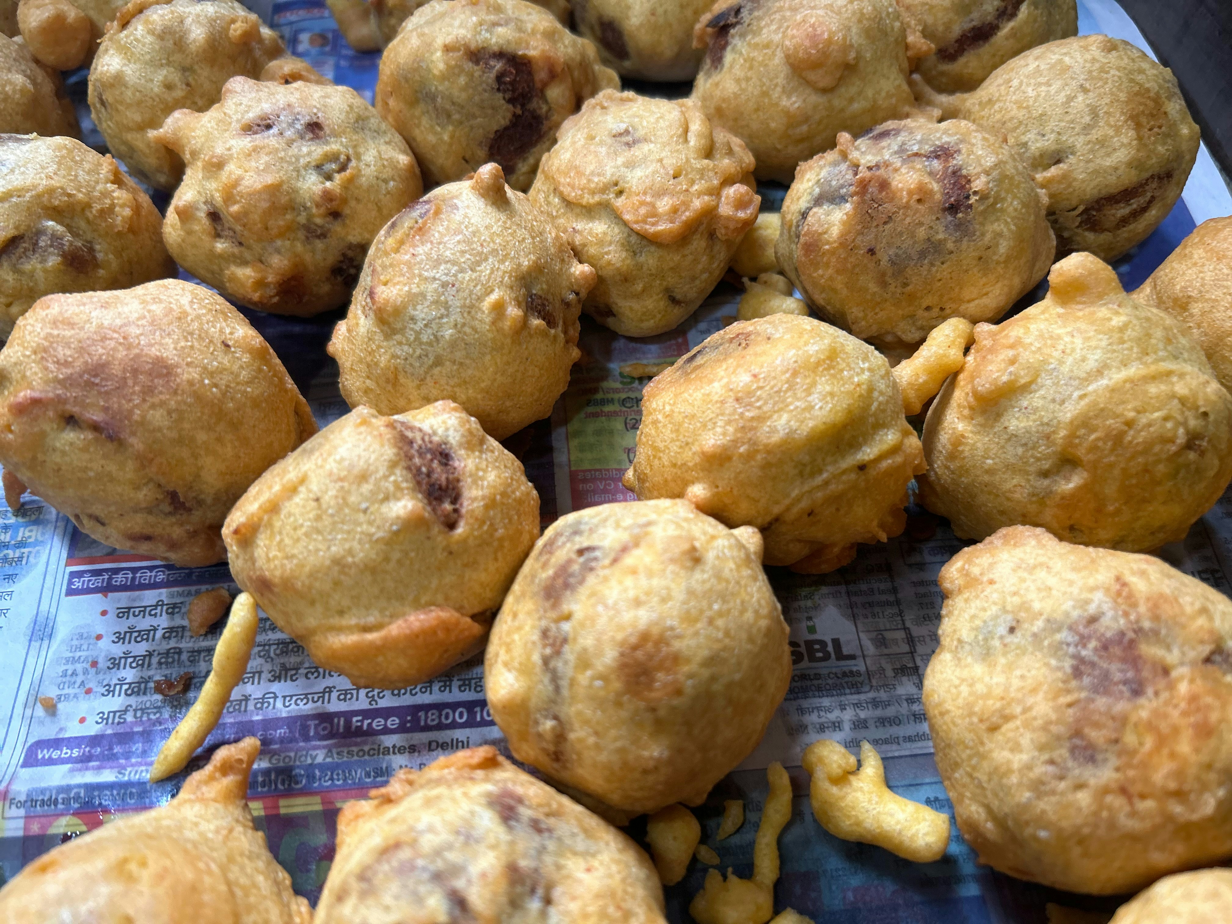 Crispy golden bhajiya fritters in a newspaper cone on a dark wooden table, evening street food vendor