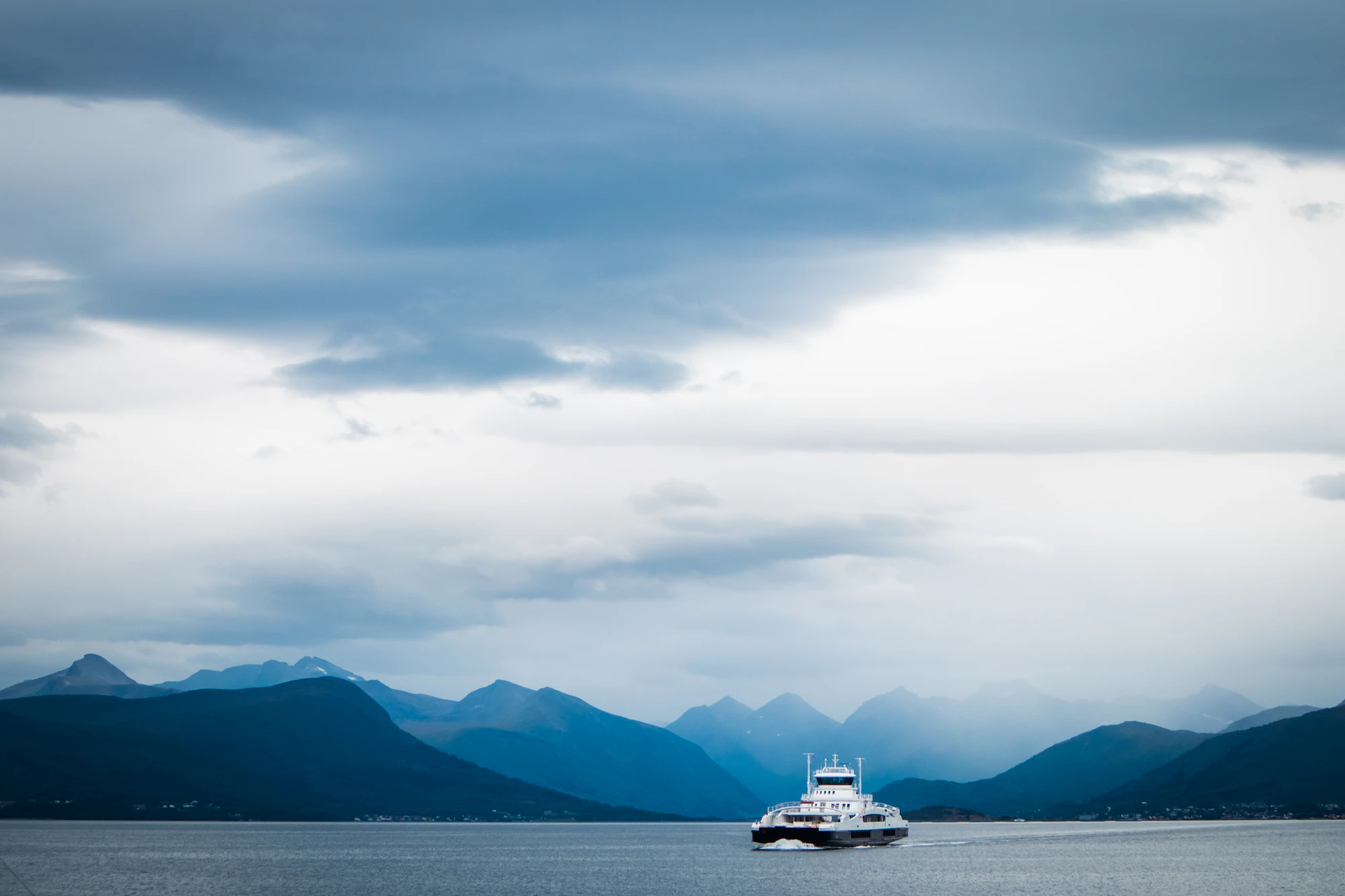 A small ferry crossing between mountains under low clouds