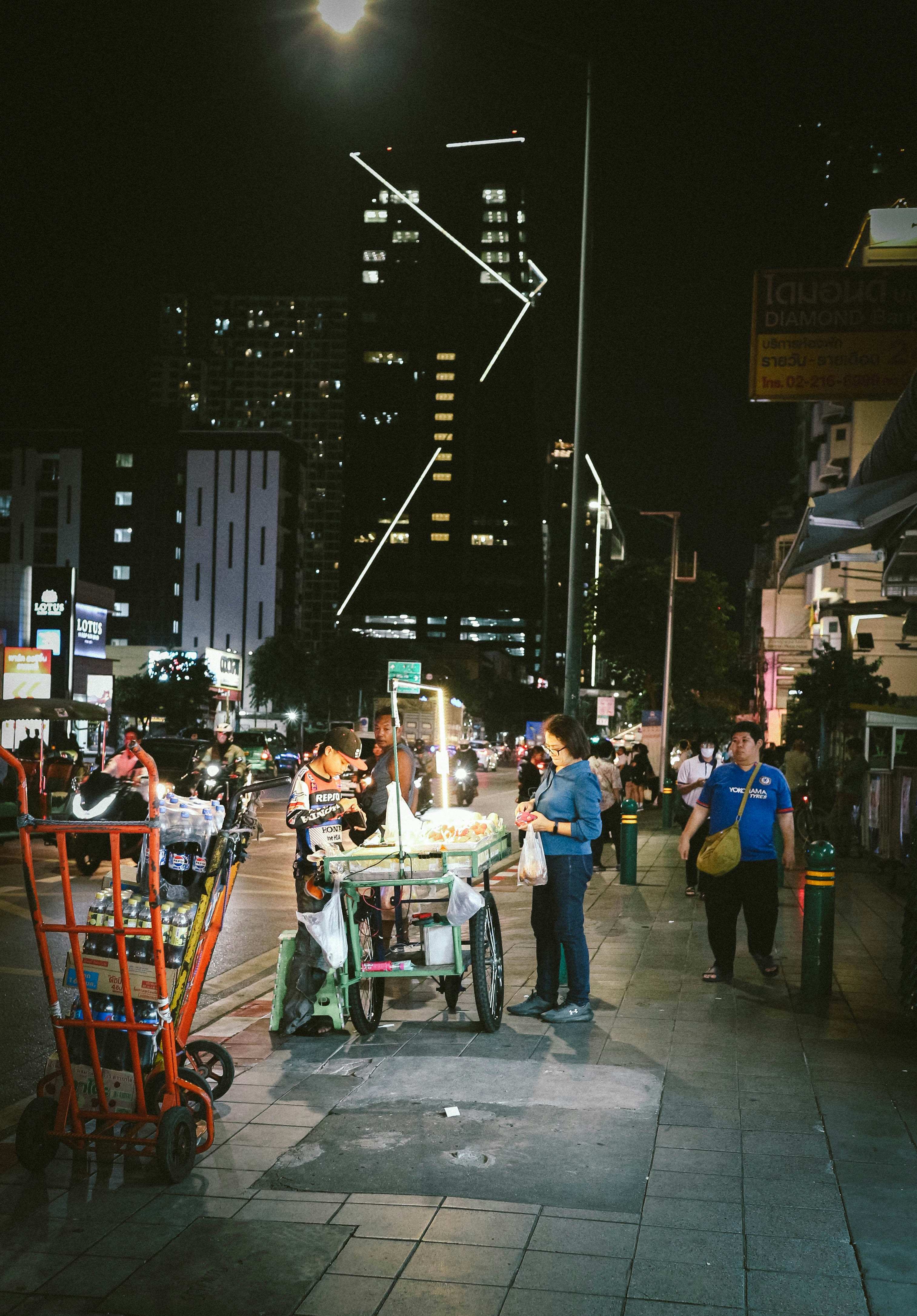A group of people standing on a sidewalk at night