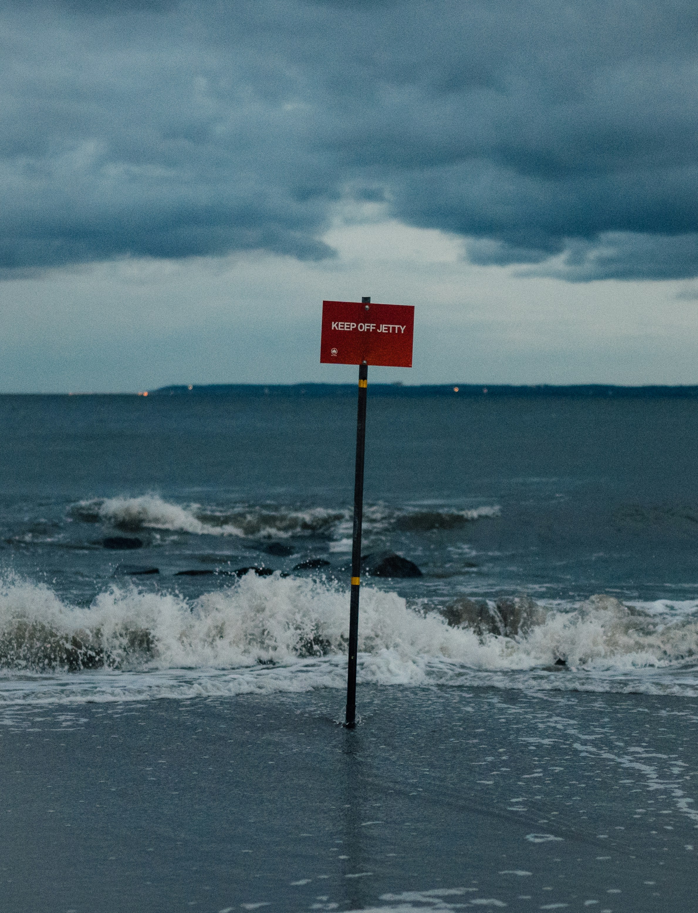 A red sign sitting on top of a beach next to the ocean photo – Free ...