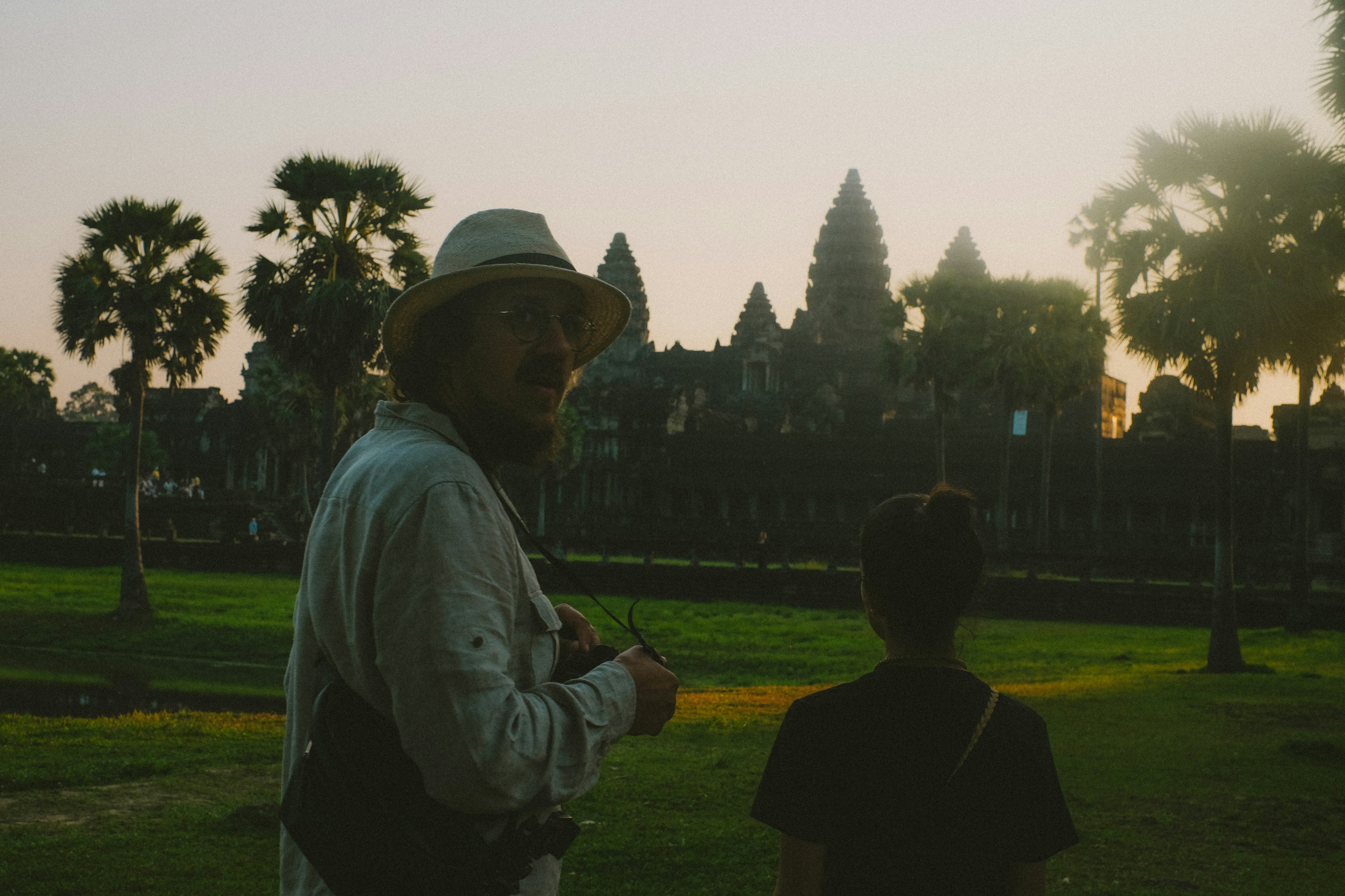 A man standing next to a little boy in a park, A photographer in front of the Angkor Wat Temples