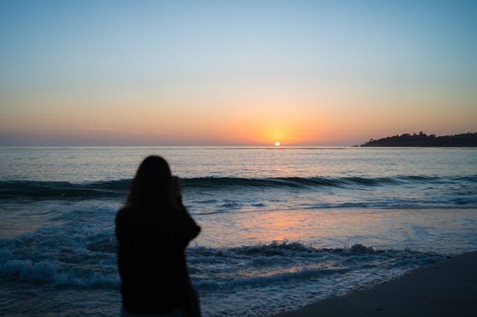A woman standing on a beach at sunset