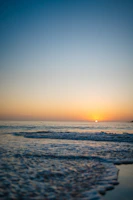 The sun is setting over the water at the beach