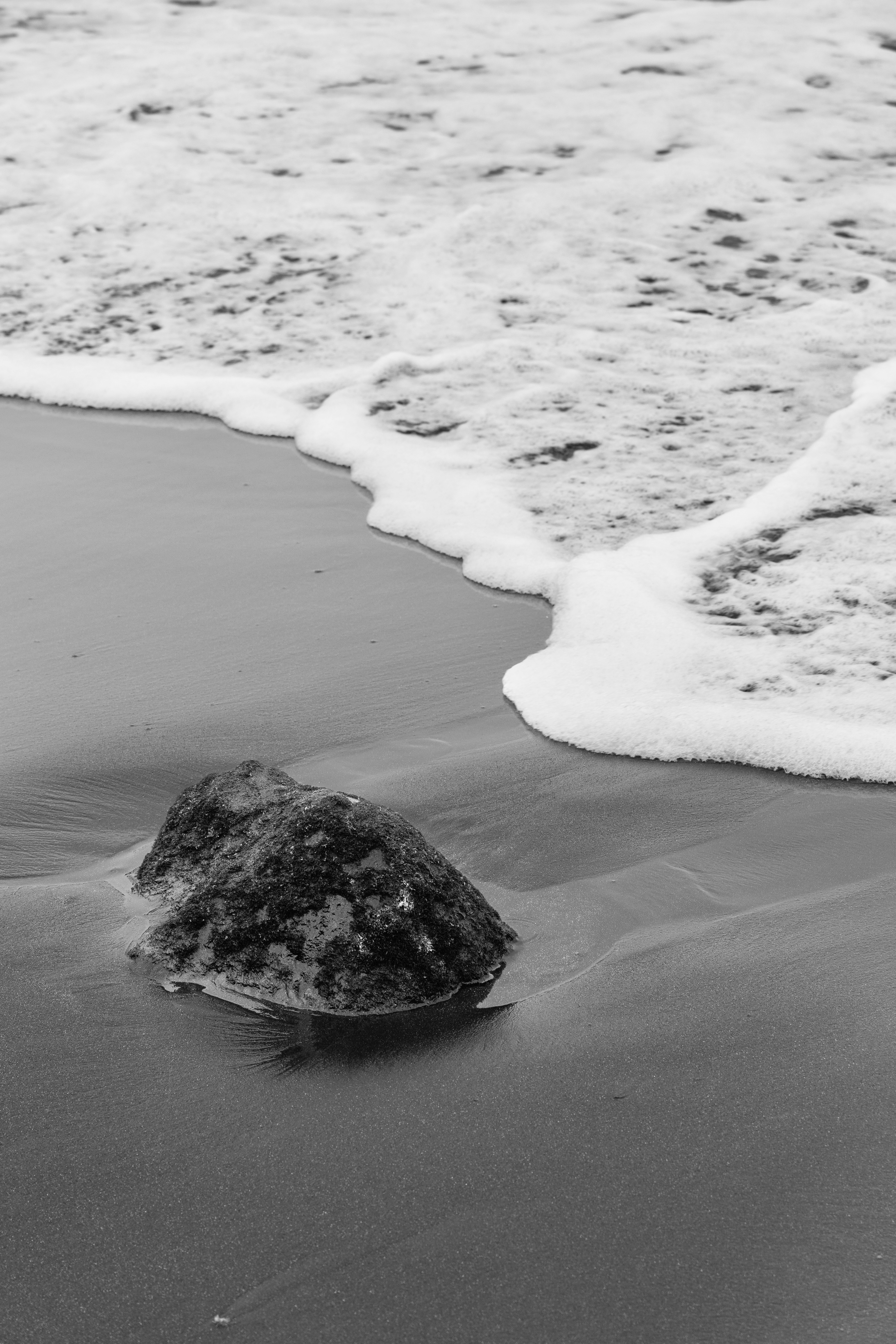 A black and white photo of a rock on the beach
