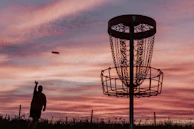 A silhouette of a man throwing a frisbee at a frisbee golf