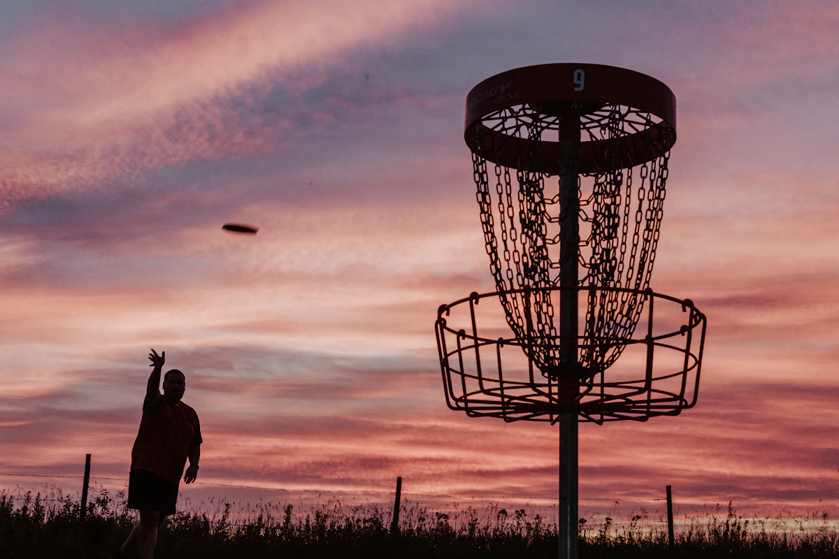 Discgolfkorg i solnedgång med kastare i bakgrunden