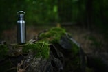 A stainless steel water bottle sitting on top of a tree stump