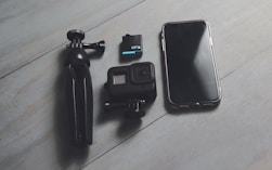 A cell phone, camera, and tripod sitting on a wooden floor