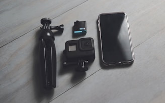 A cell phone, camera, and tripod sitting on a wooden floor