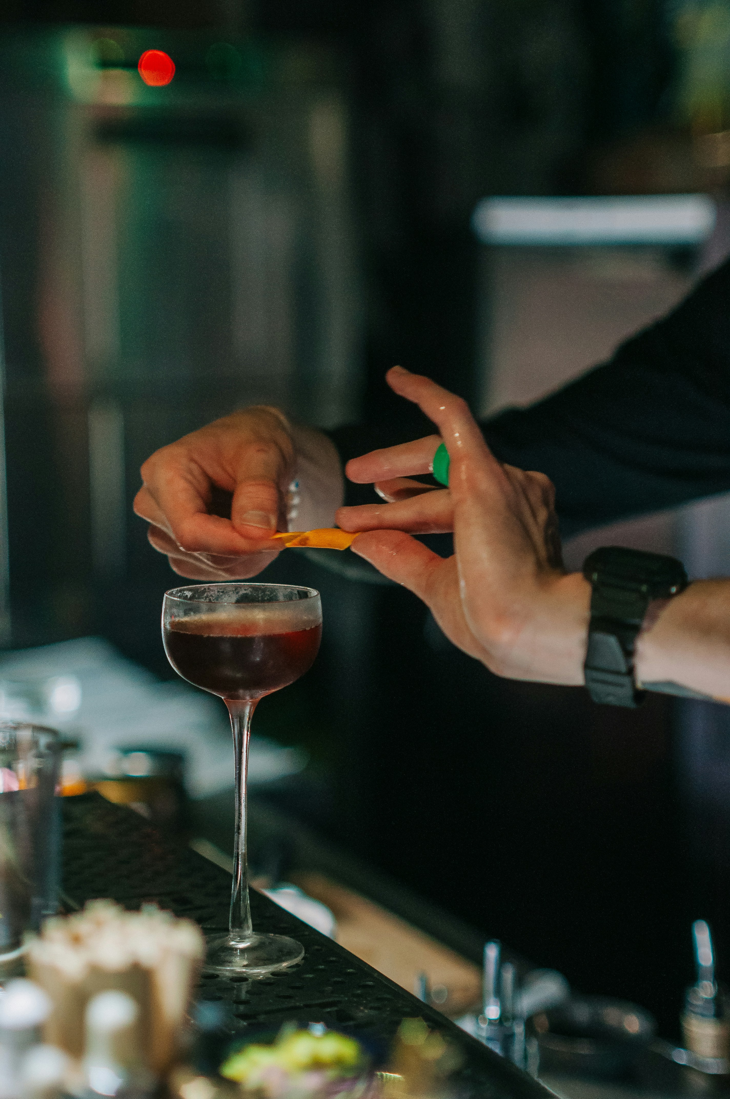 Deep red negroni cocktail with orange peel garnish and glowing neon lights reflected in the glass at Wrangler Bar Denver