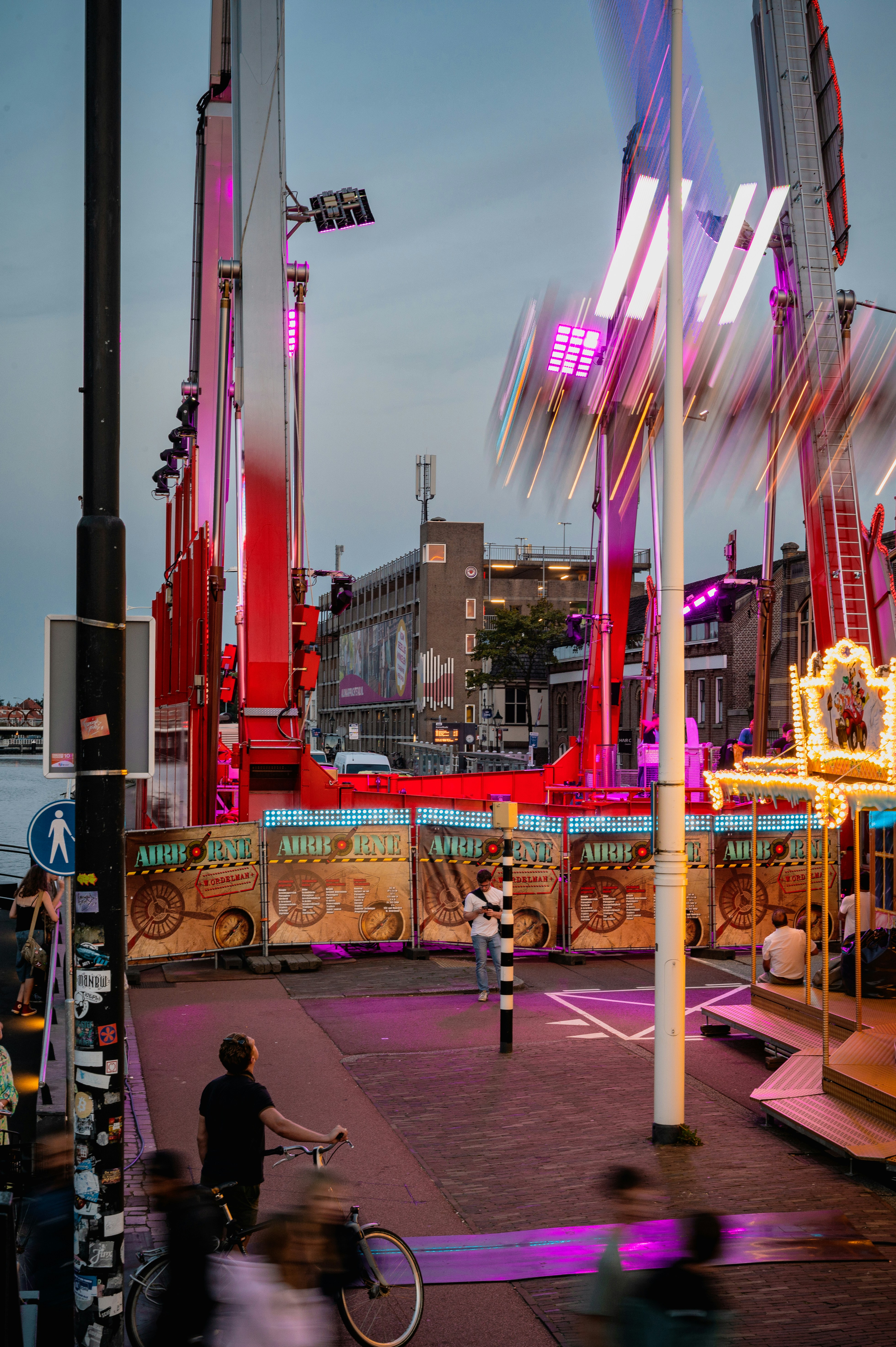 A person riding a bike down a street next to carnival rides