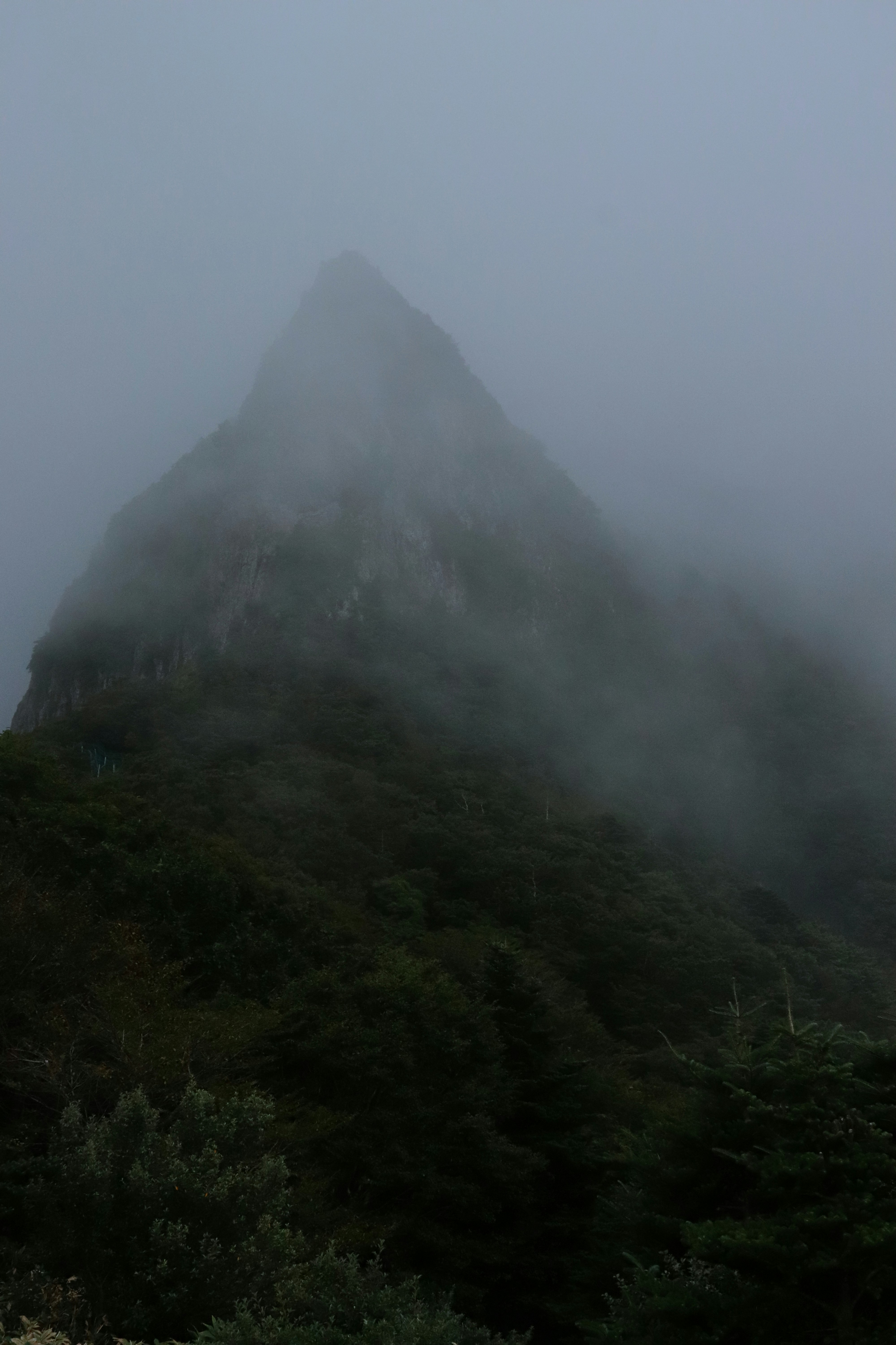 A very tall mountain covered in fog on a cloudy day