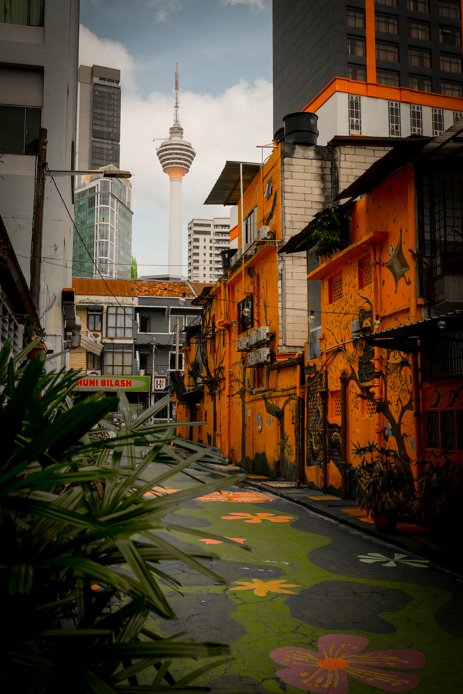 Narrow colourful lane with murals and painted ground, KL Tower visible in the distance