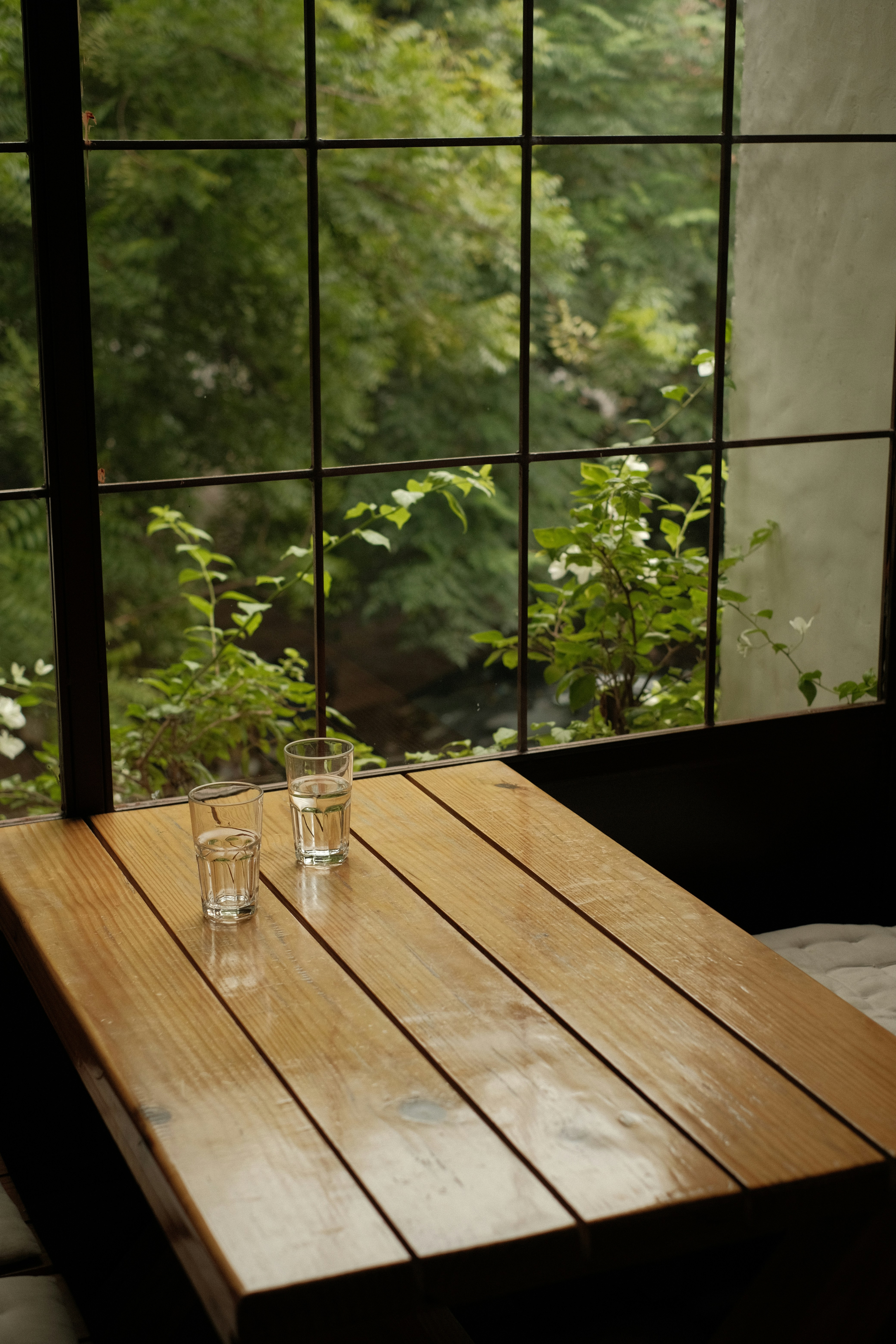 Two glasses of water on a slatted table by a window.