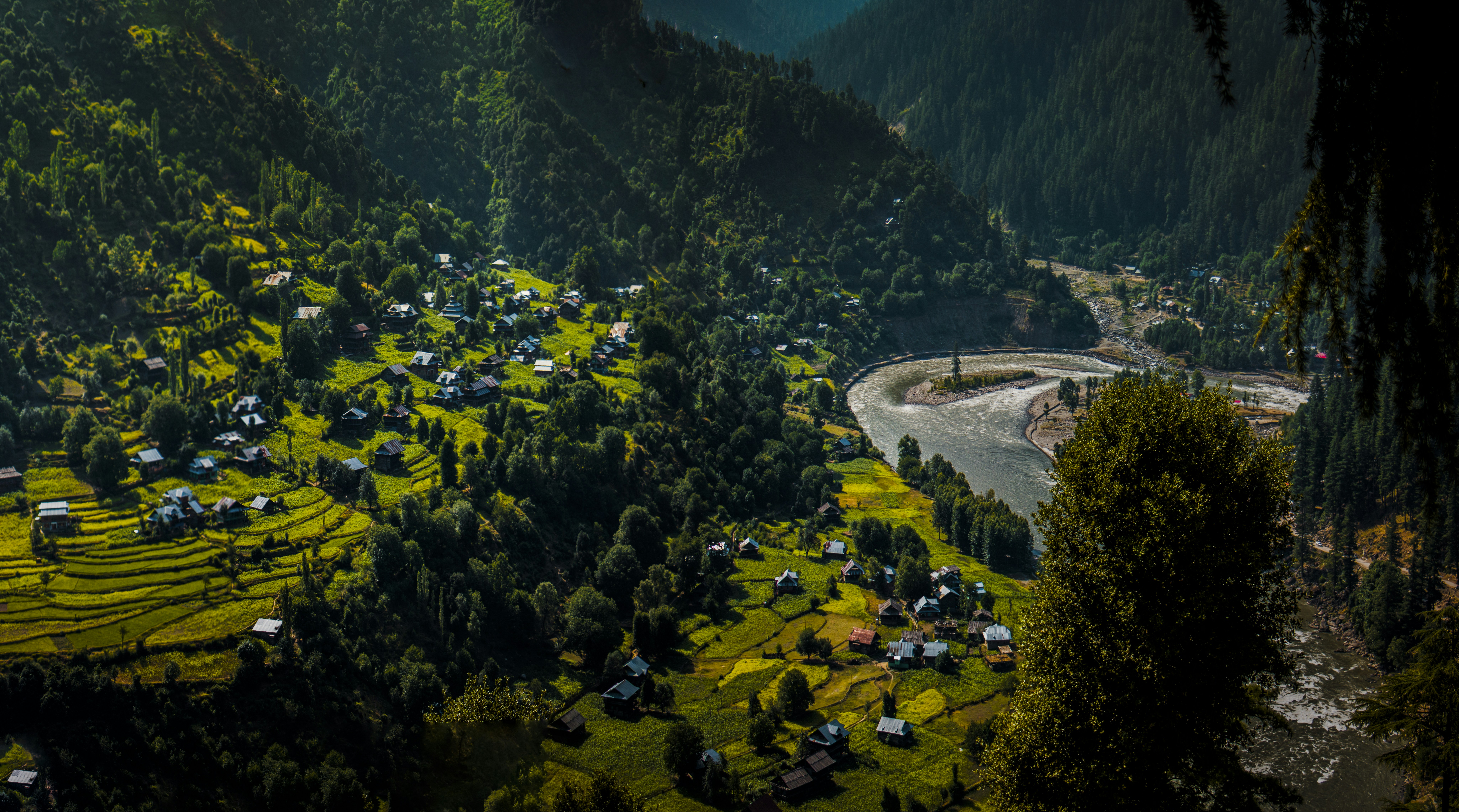An aerial view of a mountainous, rugged terrain with scattered small villages, representing the challenging geography of Pakistan-occupied Kashmir.