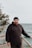 A man in a black hoodie standing on a wooden deck next to the ocean