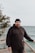 A man in a black hoodie standing on a wooden deck next to the ocean