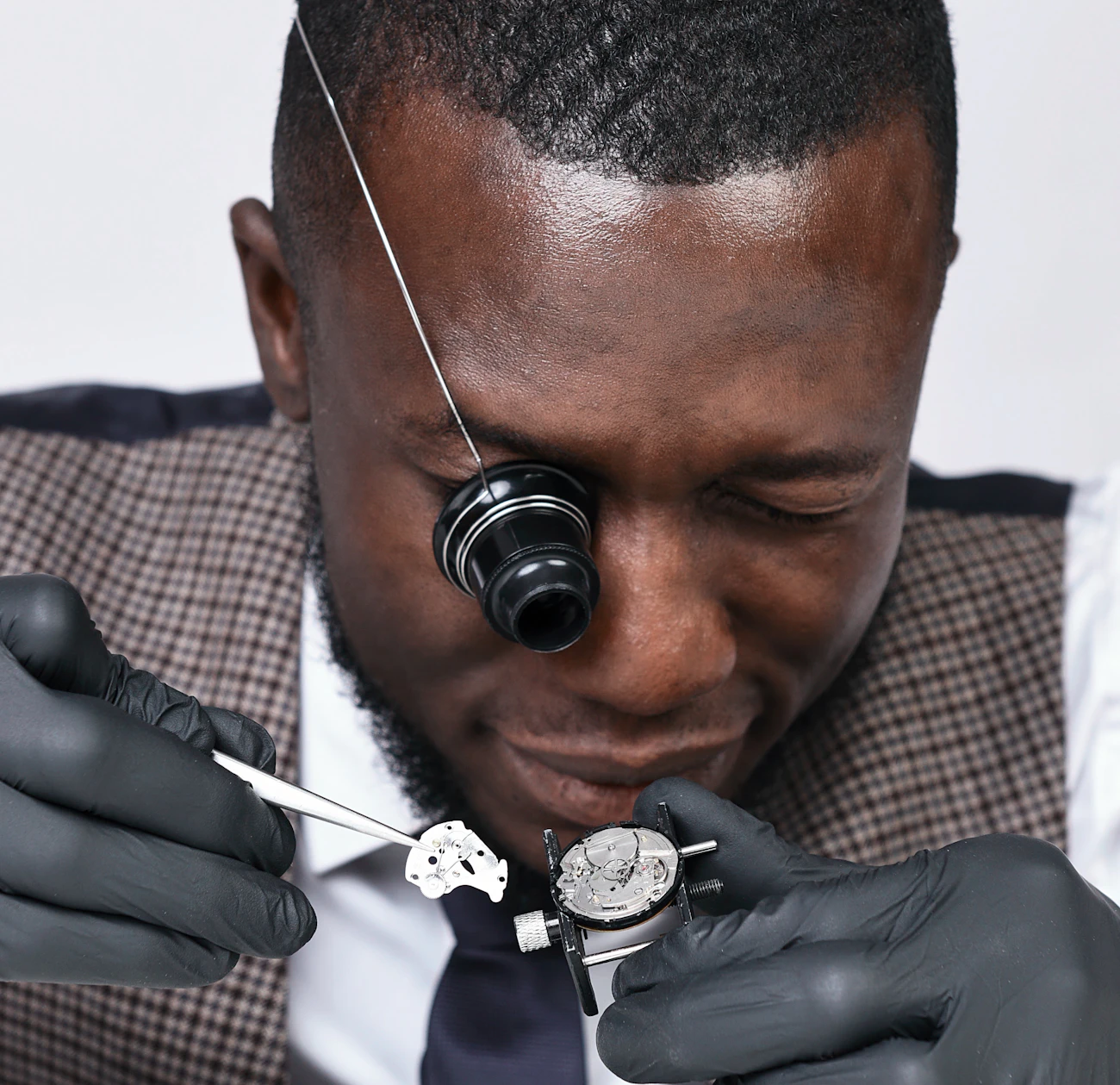 Watchmaker using a loupe and tweezers to repair the movement of a wristwatch