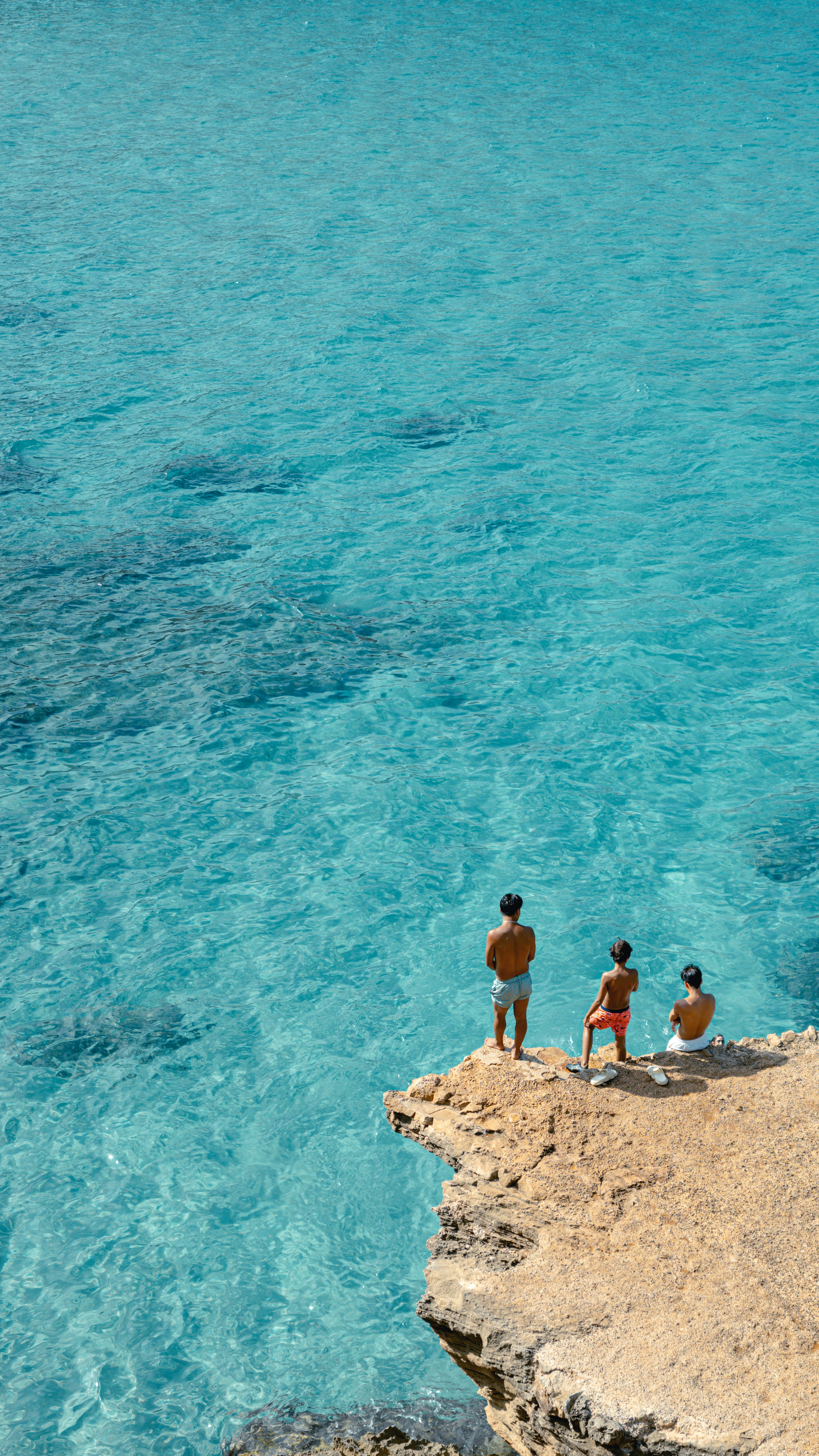 A group of people standing on top of a cliff next to a body of water ...